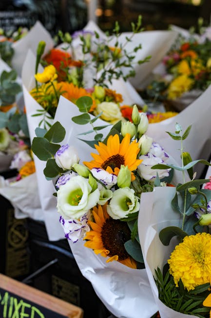 A vibrant floral arrangement featuring a mix of fresh sunflowers with bright yellow petals and dark centers, complemented by white and purple lisianthus with delicate, ruffled petals and green buds. T
